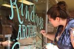 Mizzou alumna Beth Snyder painting hand lettering on a store window