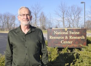 A photo of Randall Prather in front of a sign for the National Swine Resource & Research Center.