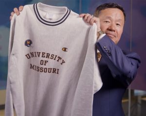 A photo of President Choi holding a gray sweatshirt that says University of Missouri.