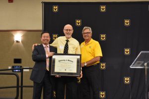 A photo of President Choi and Curator Keith Holloway present Coach Busch with the Chancellor’s Award for Lifetime Achievement.