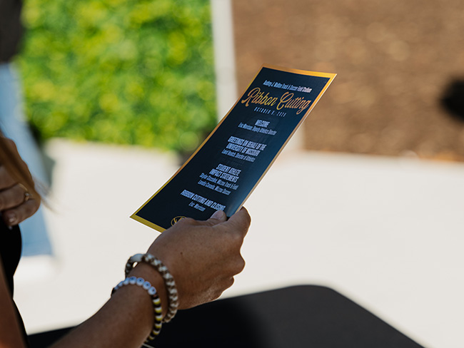 A woman holds a program for the 2026 Audrey J. Walton Track & Soccer Field Stadium Ribbon Cutting